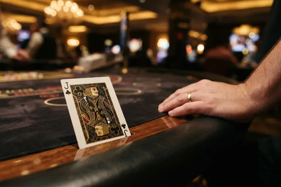 Casinos sin licencia España: jota de tréboles apoyada en una mesa de casino junto a la mano de un jugador